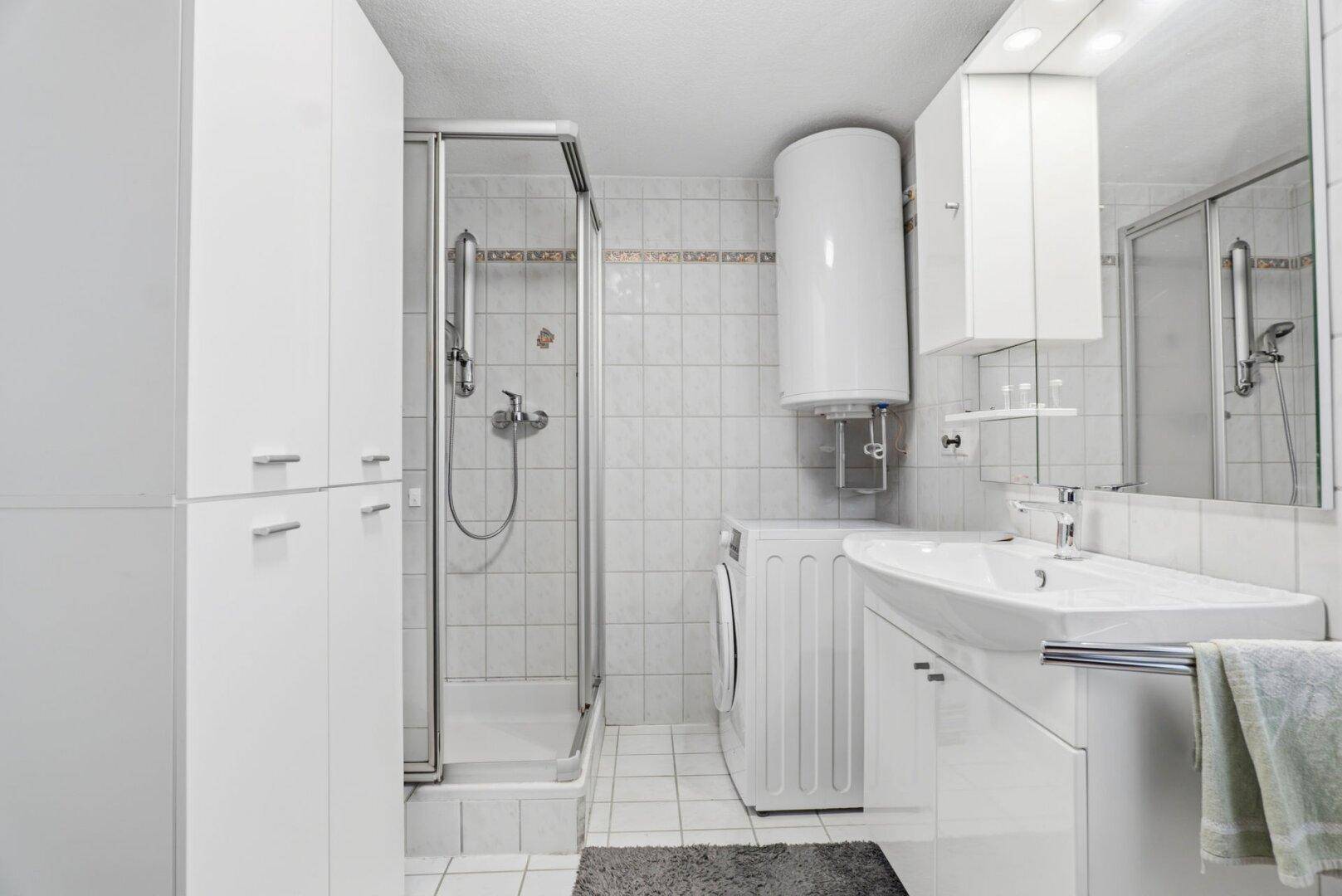 Badezimmer mit Duschkabine, Waschmaschine und weiß gefliesten Wänden.