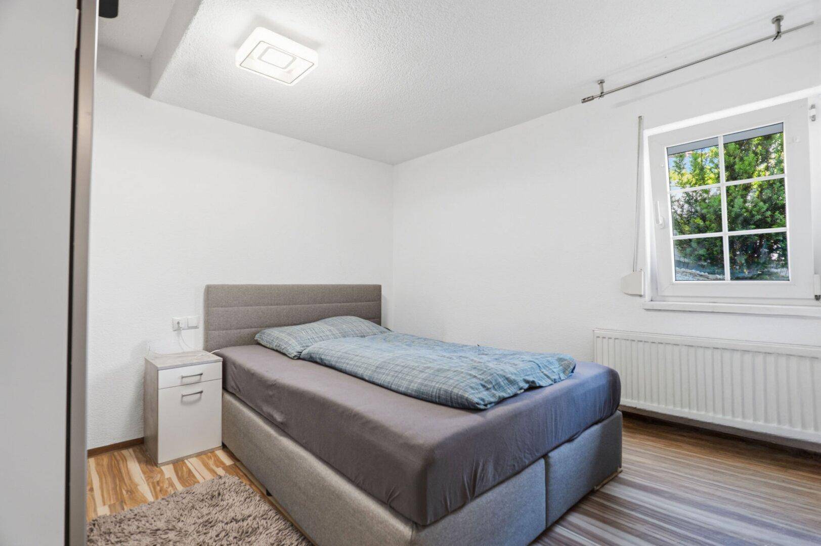 Schlafzimmer mit Einzelbett, Laminatboden und Fenster mit Blick ins Grüne.