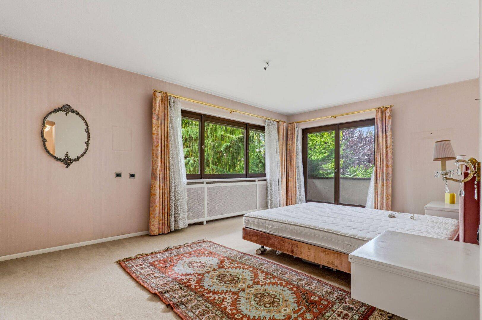 Helles Schlafzimmer mit großen Fenstern, Teppichboden und Blick auf die umliegende Natur.