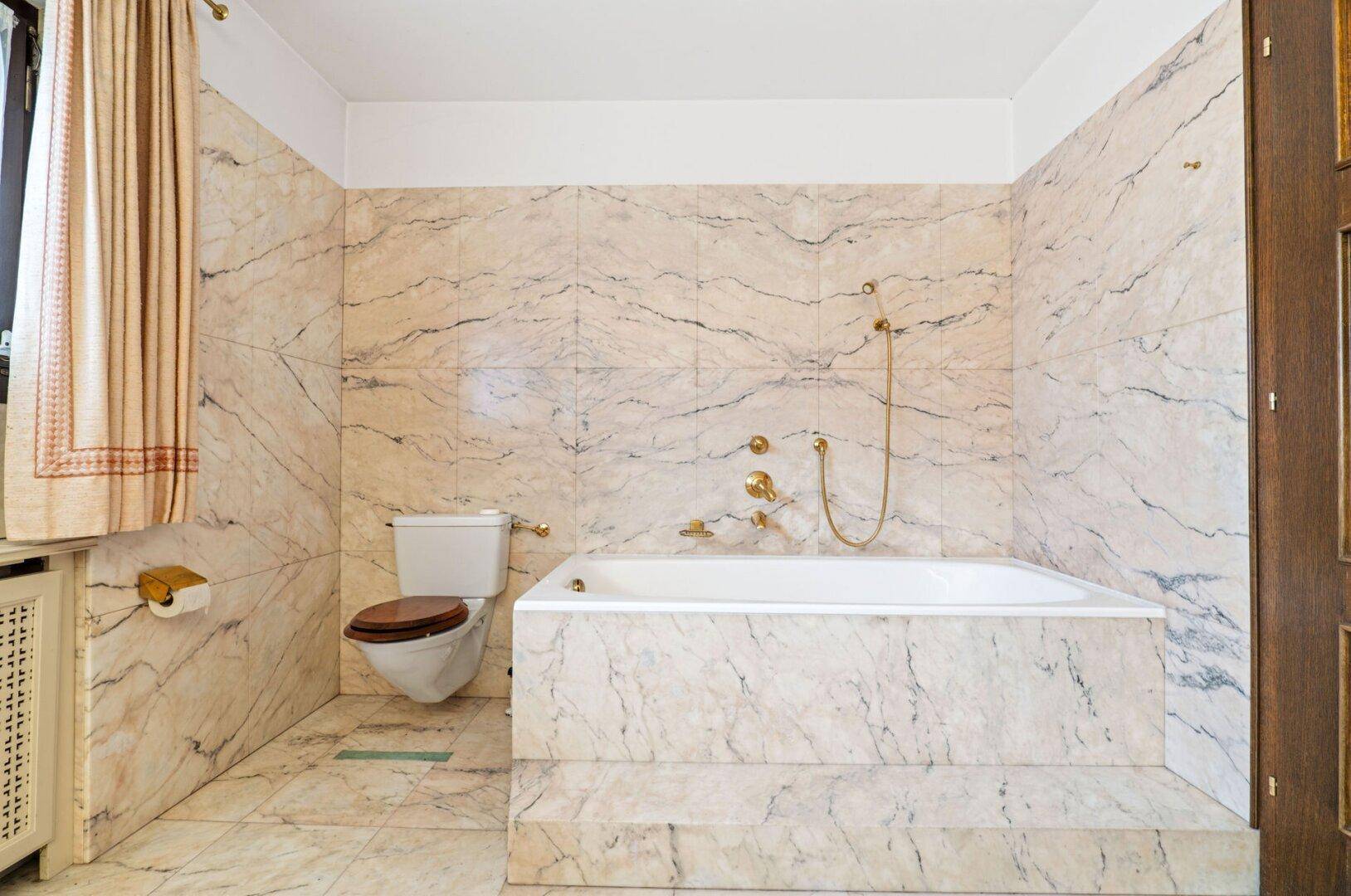 Badezimmer mit eleganten Marmorfliesen, integrierter Badewanne und goldenen Armaturen.
