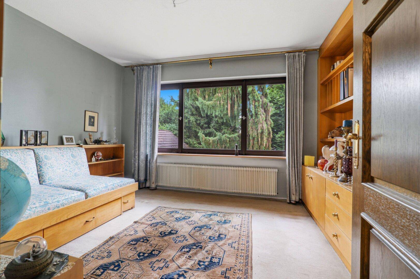 Helles Zimmer mit Sofa, Bücherregalen und weitem Blick in die grüne Umgebung.