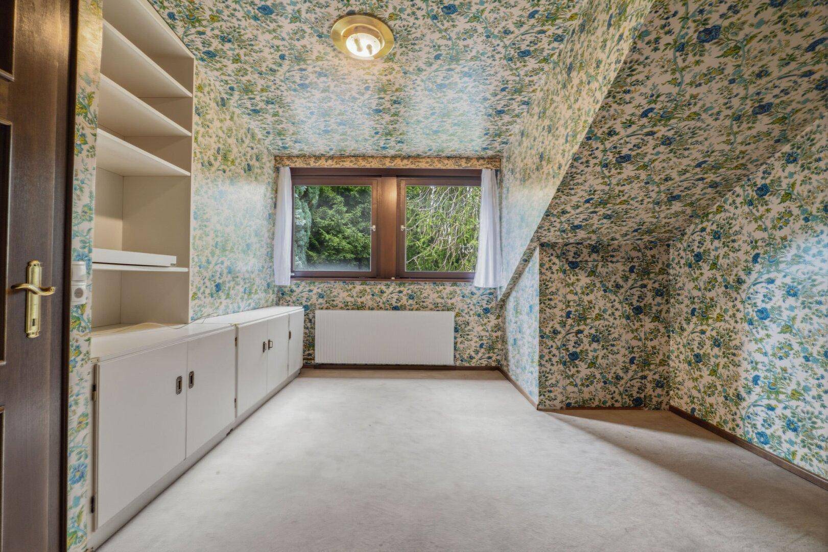 Dachzimmer mit auffälliger Blumen-Tapete, Dachschräge und praktischen Einbauschränken.