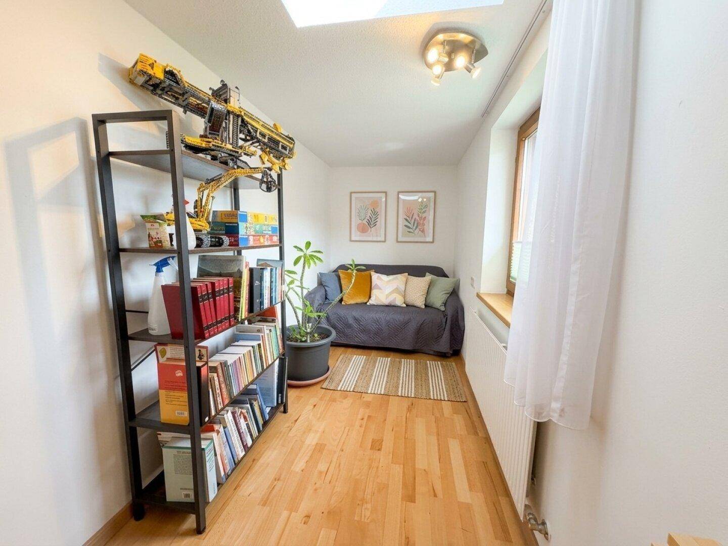 Kleines, helles Zimmer mit Sofa, Regal und Fenster, ideal als Büro oder Gästezimmer.