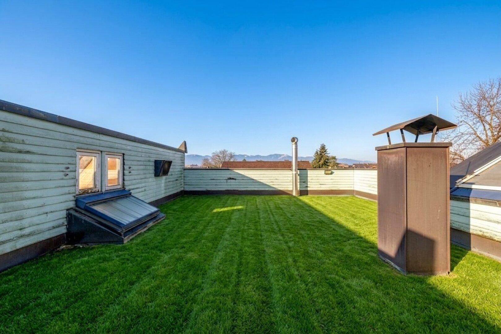 Weitläufige Dachterrasse mit Rasenfläche und Blick auf die umliegende Landschaft und Berge.