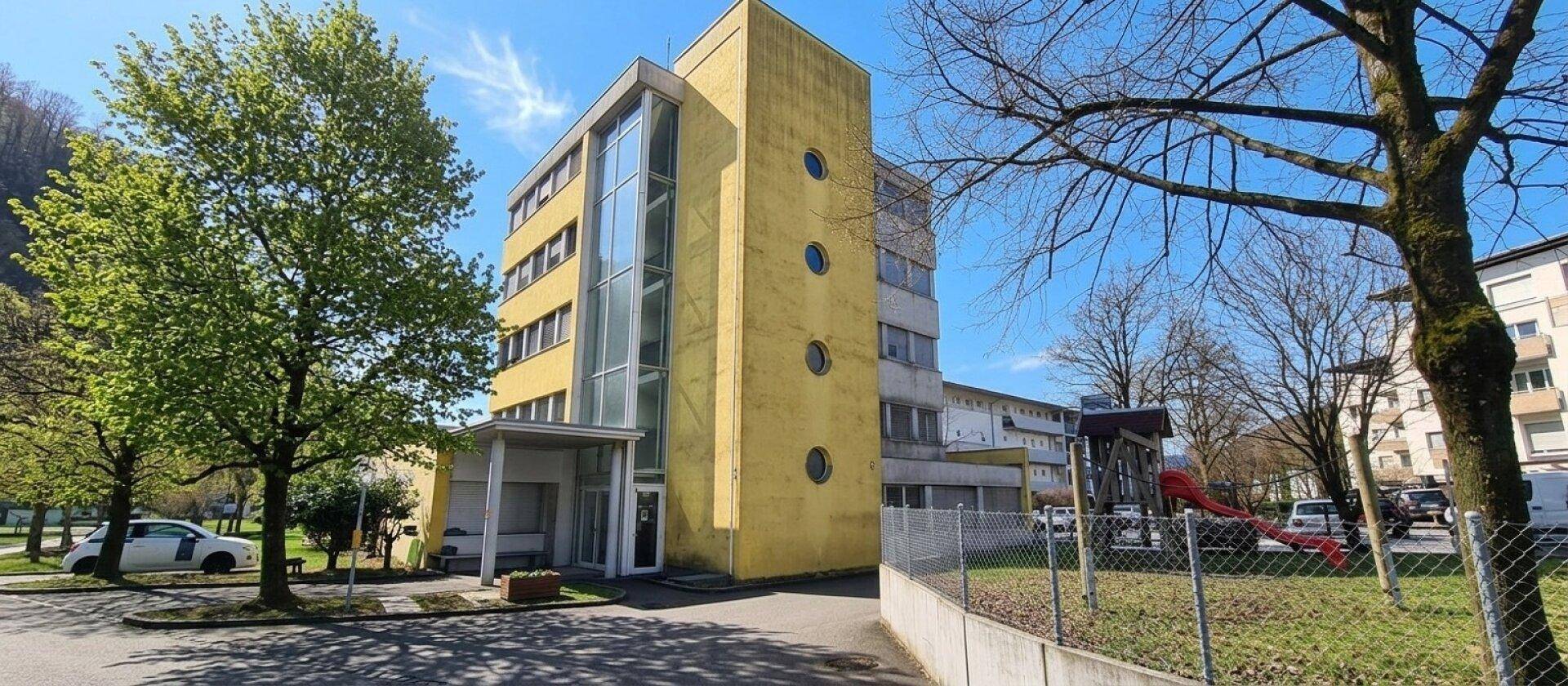 Modernes Gebäude mit gelber Fassade, großen Glasflächen und einem Spielplatz in der Nähe.