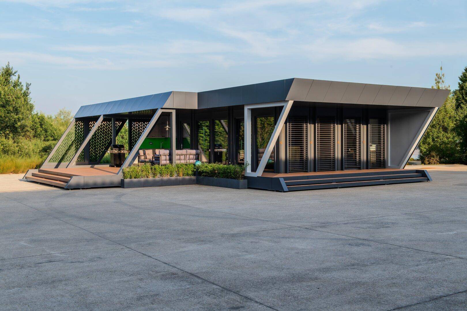 Modernes Gebäude mit markanter Architektur, kleiner Terrasse und großzügiger gepflasterter Fläche.