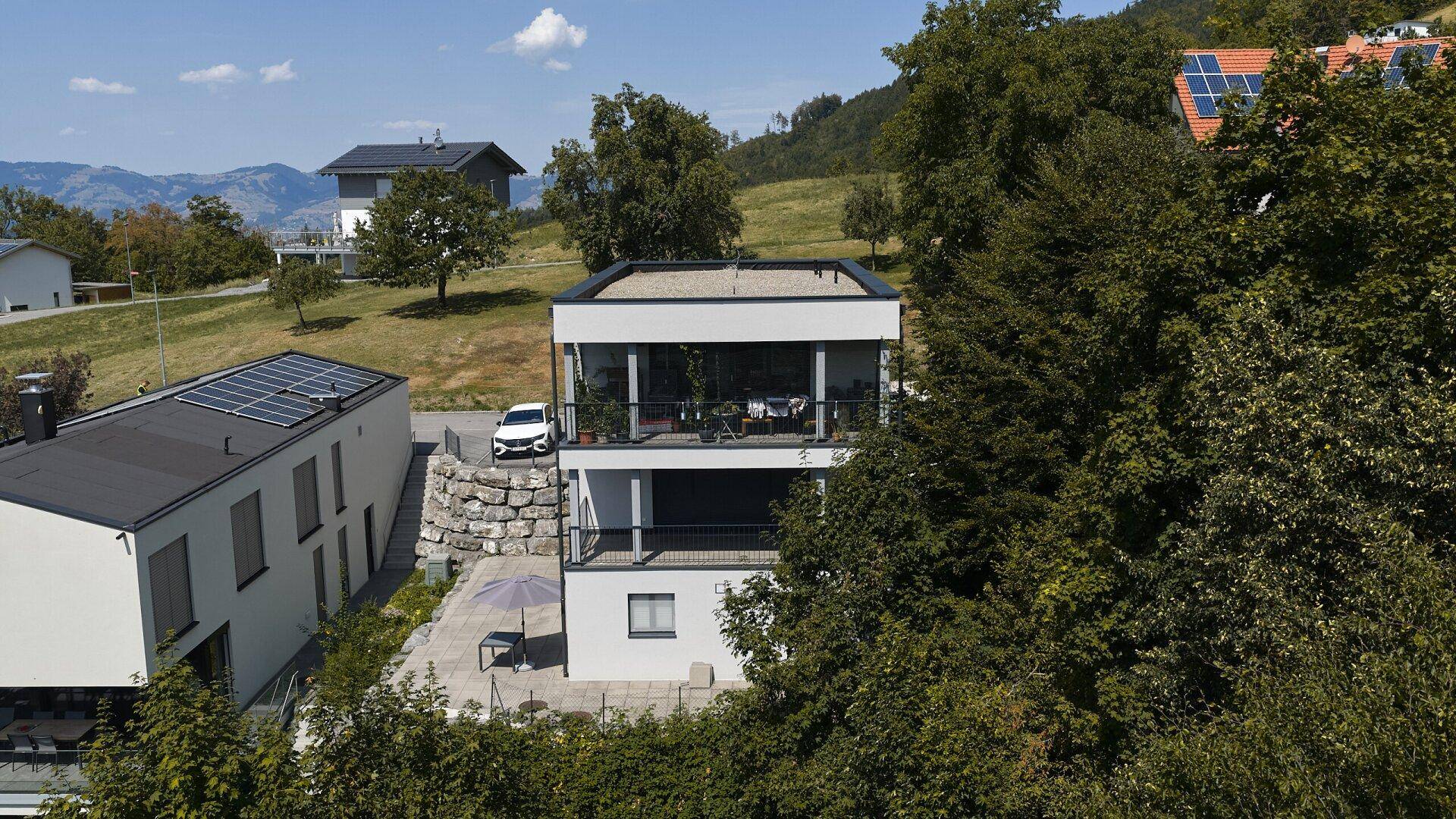 Moderne Wohngebäude mit Flachdach und großen Fensterfronten, umgeben von üppiger Vegetation.