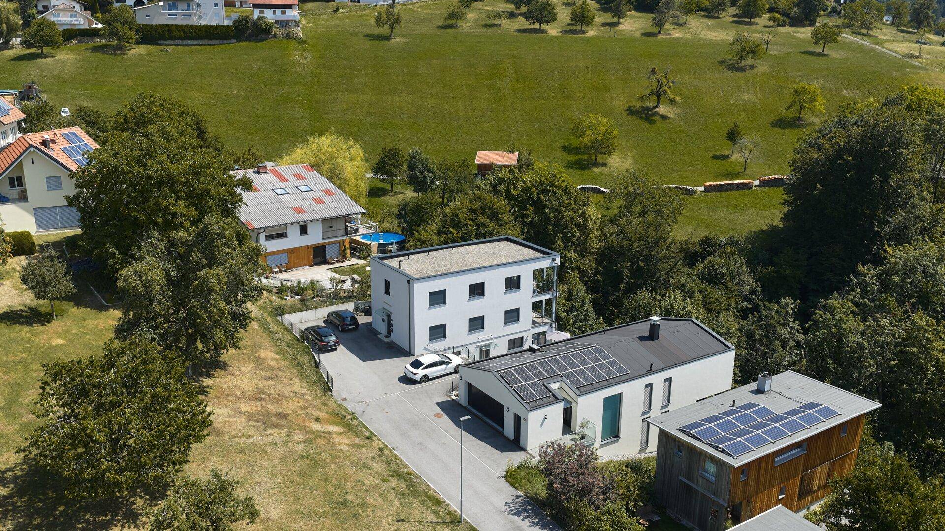Überblick über mehrere moderne Gebäude in einer ländlichen Umgebung mit viel Grün und weiteren Häusern.