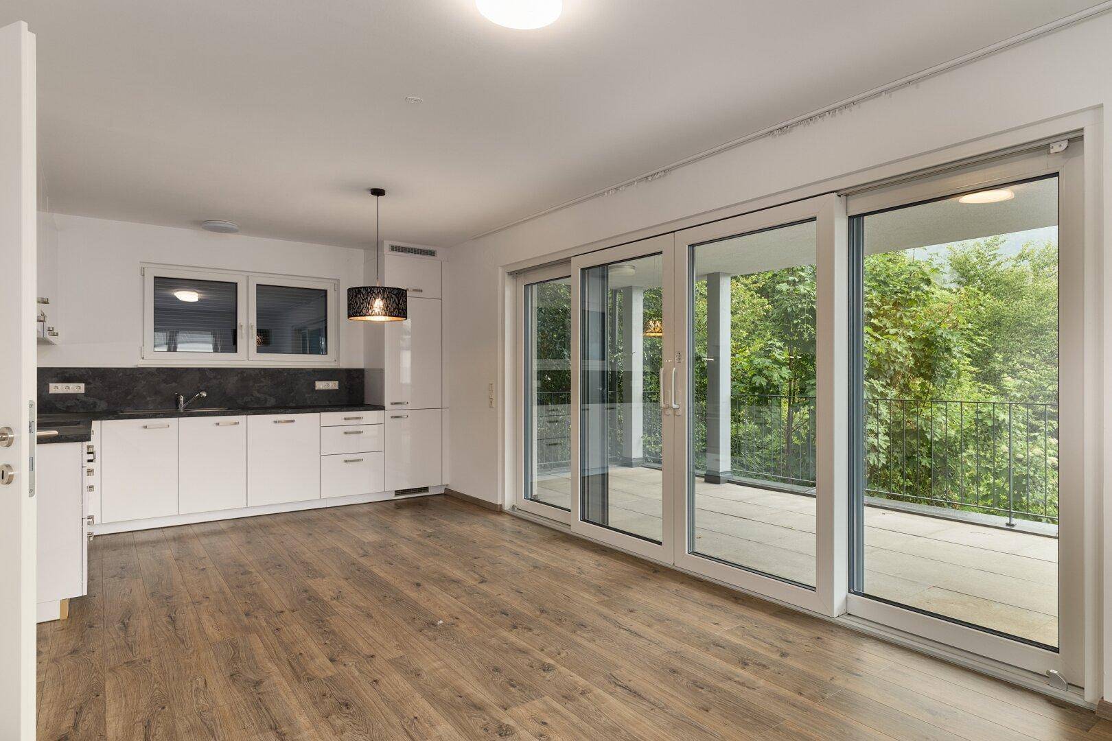 Heller offener Wohnbereich mit integrierter Küche, Holzboden und Zugang zu einer großen Terrasse.