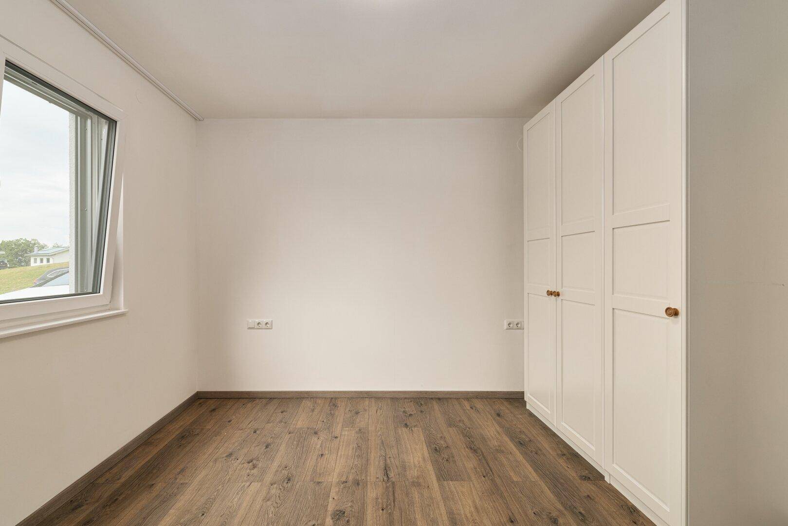 Helles Schlafzimmer mit Laminatboden und einem weißen Kleiderschrank, ideal als Kinder- oder Gästezimmer.