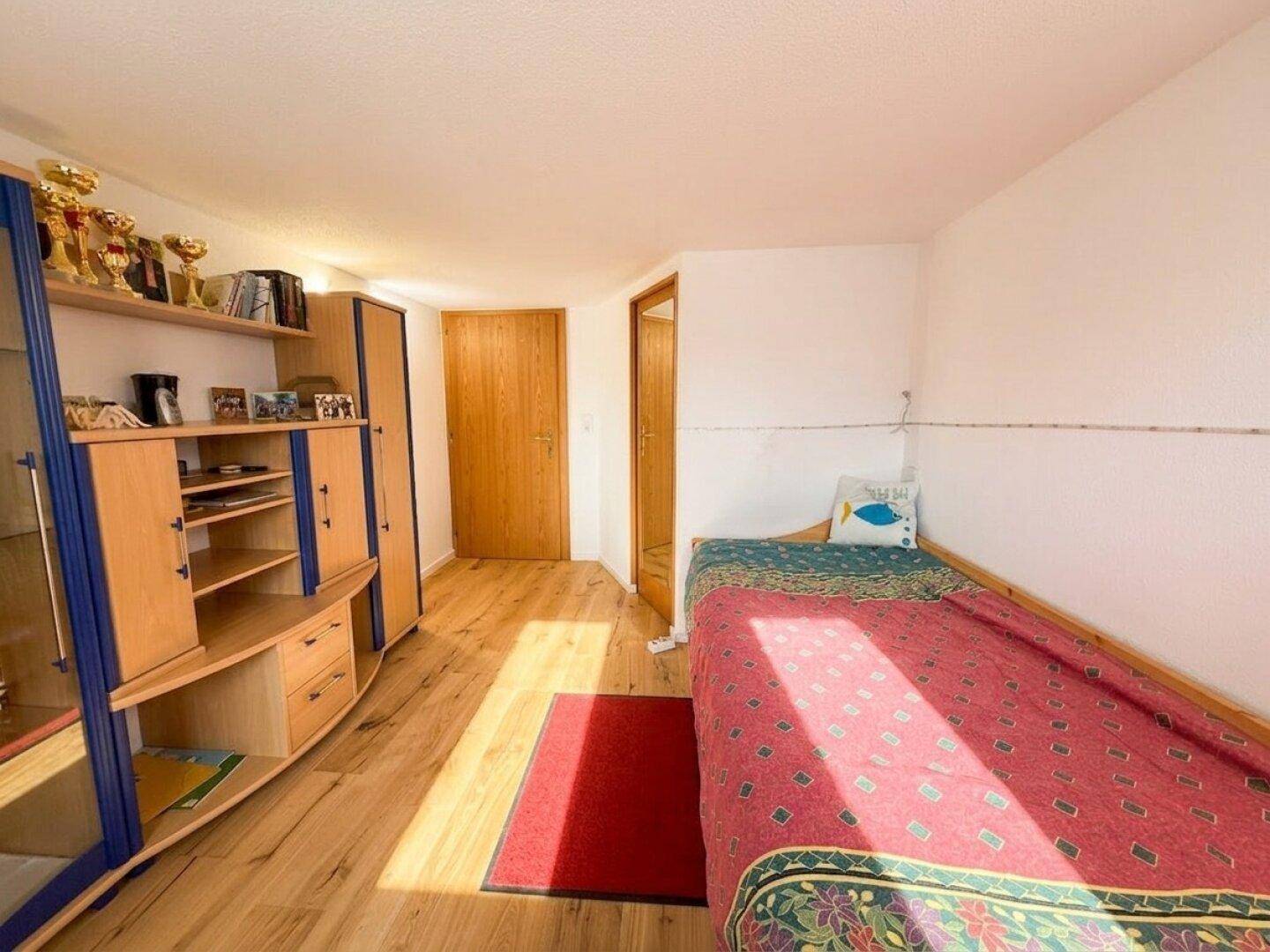 Kinderzimmer mit Holzboden, Bett und Schrank, hell und freundlich gestaltet.
