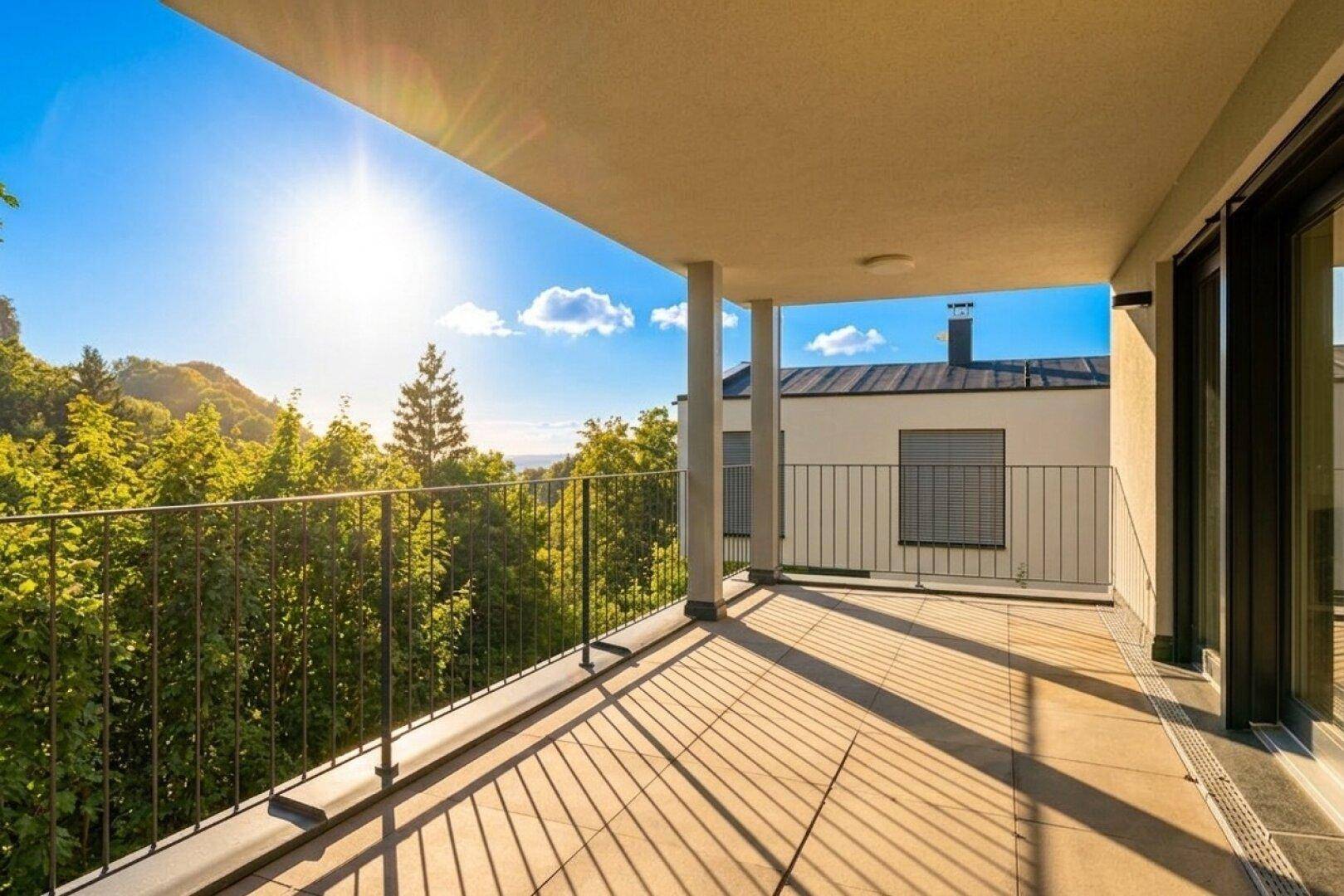Sonniger Balkon mit Fliesenboden, Metallgeländer und weitem Blick über grüne Baumwipfel.