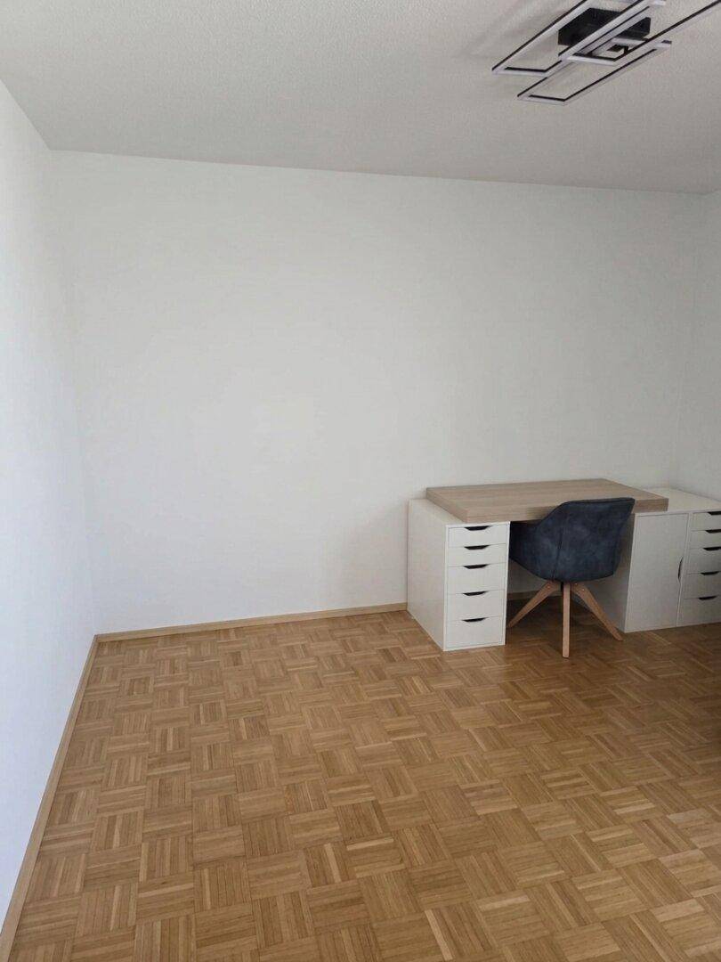 Helles Zimmer mit Parkettboden und einem Schreibtisch, ideal als Büro oder Arbeitszimmer.
