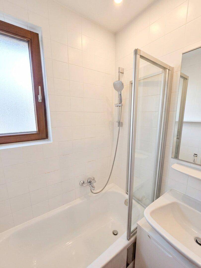Badezimmer mit Badewanne, Duschabtrennung, Waschbecken und einem Fenster für natürliches Licht.