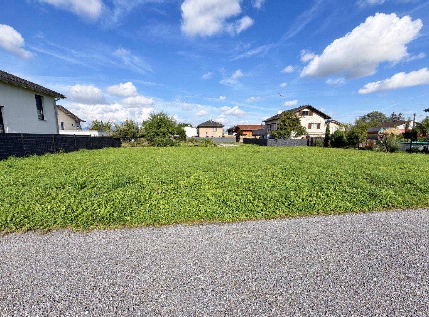 Großes unbebautes Grundstück mit grüner Wiese, umgeben von Wohnhäusern und klarem Himmel.
