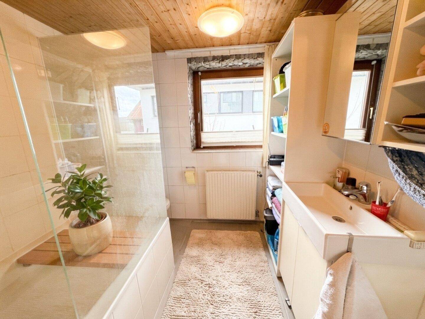 Badezimmer mit Duschkabine, Waschbecken und Fenster, das Tageslicht hereinlässt.