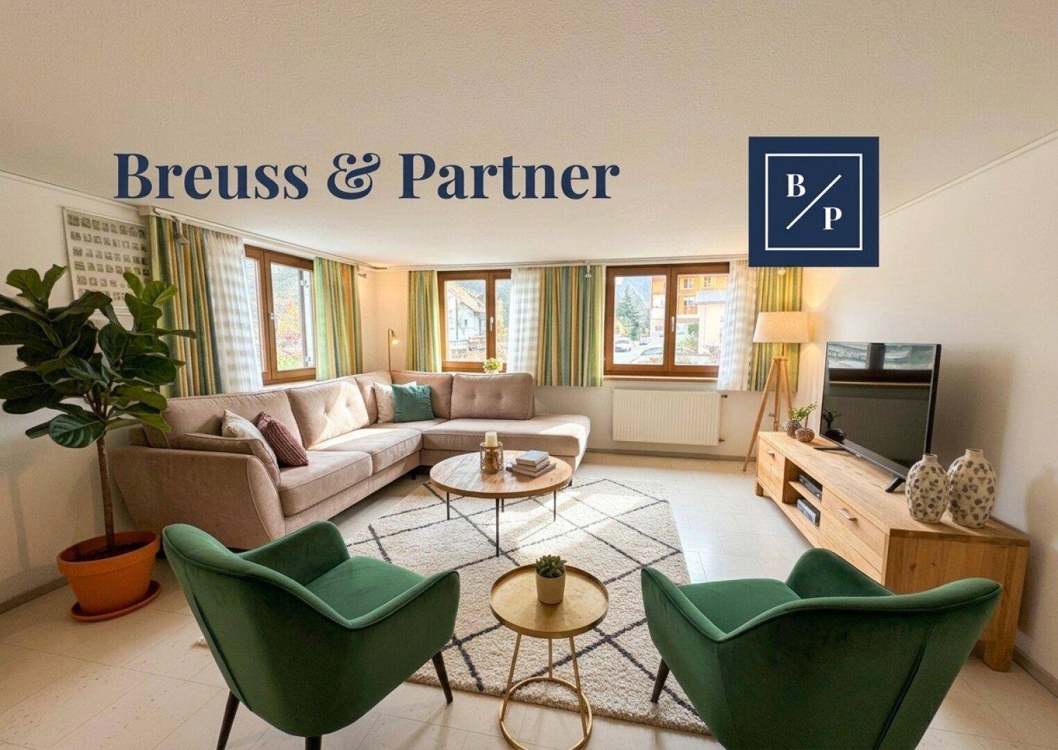 Helles Wohnzimmer mit beigem Ecksofa, zwei grünen Sesseln und Blick nach draußen.