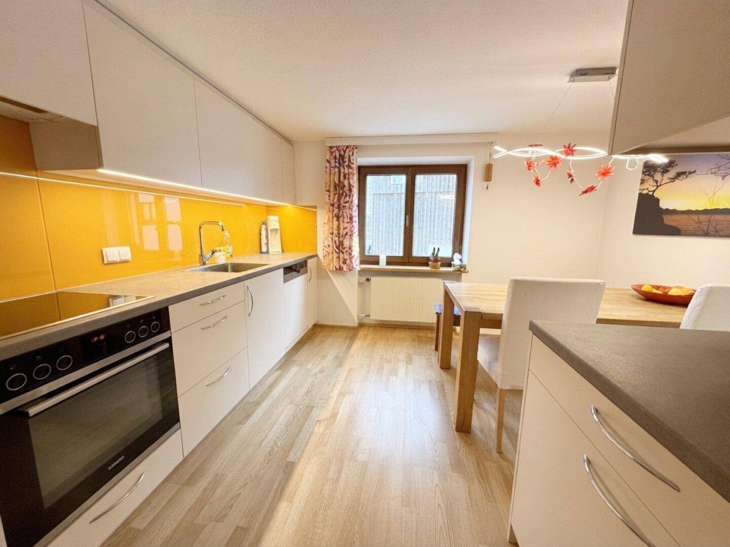 Moderne Küche mit weißen Schränken, gelber Rückwand und Essbereich mit Holztisch.