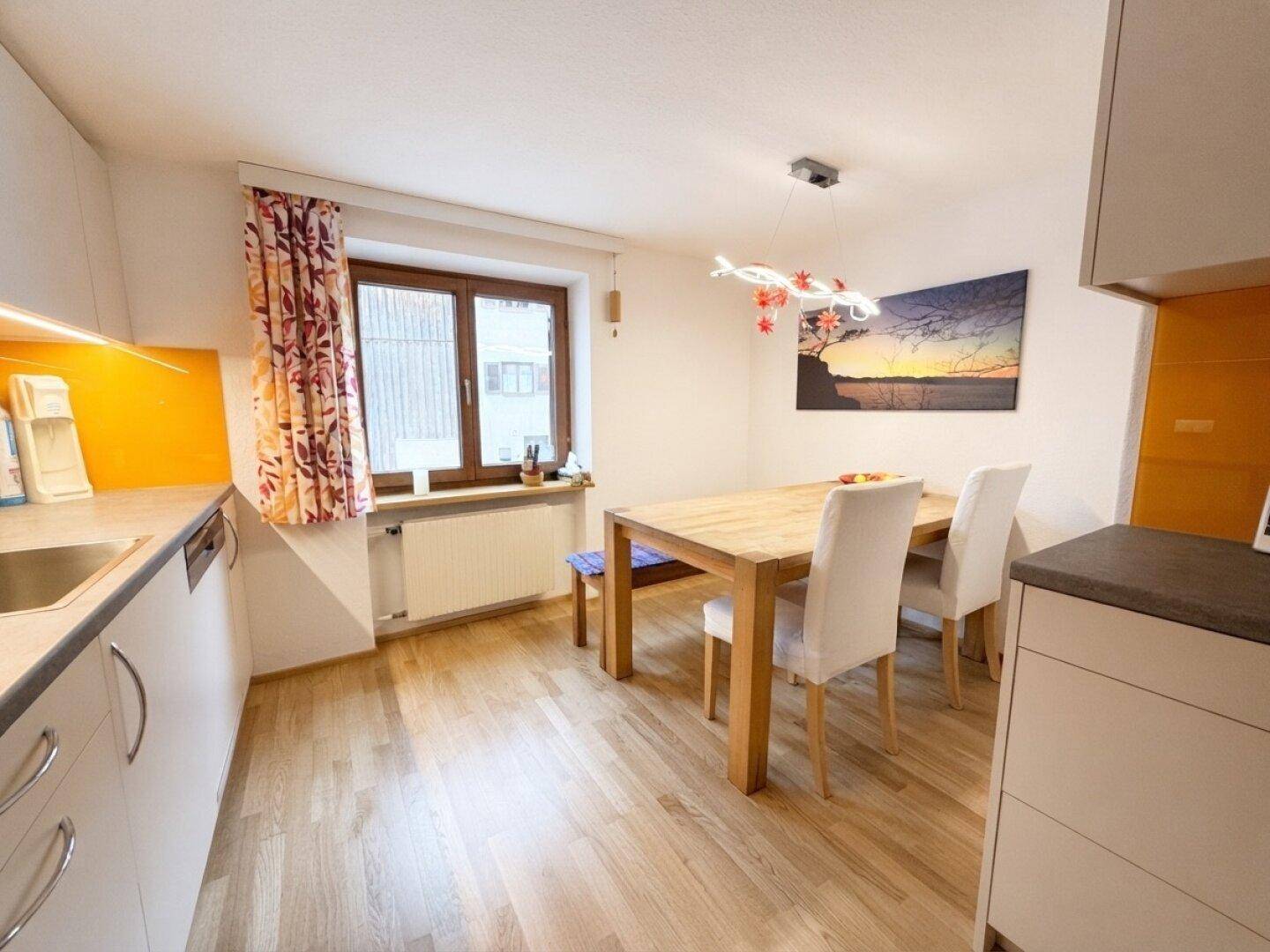 Heller Essbereich in der Küche mit Holztisch und Stühlen, beleuchtet durch ein Fenster.