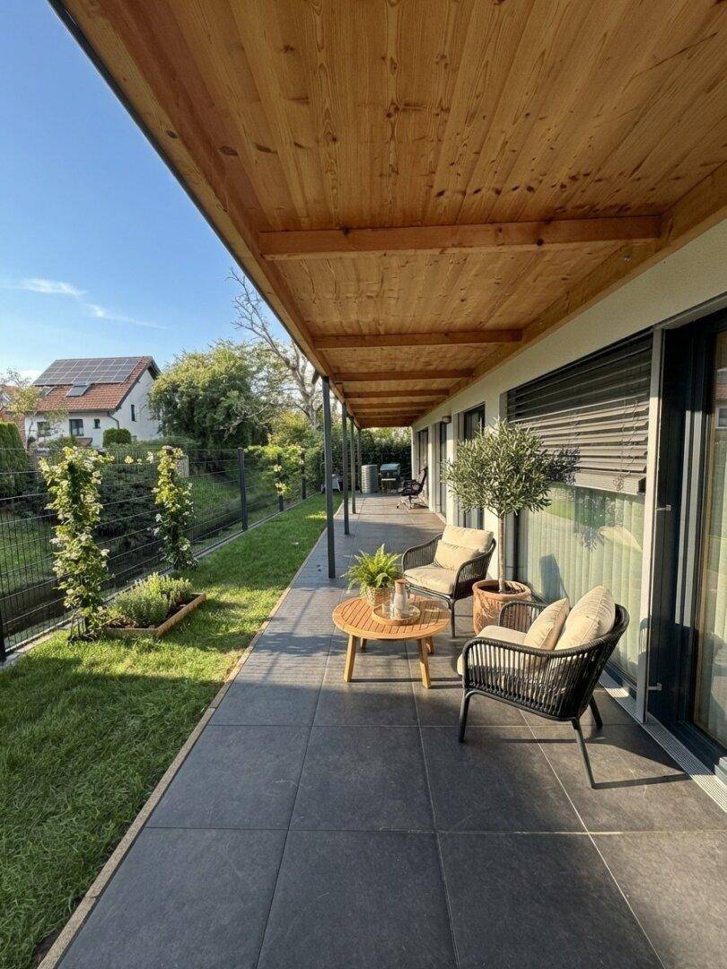 Lange überdachte Terrasse mit Sitzgelegenheiten, Rasenfläche und Bergblick.