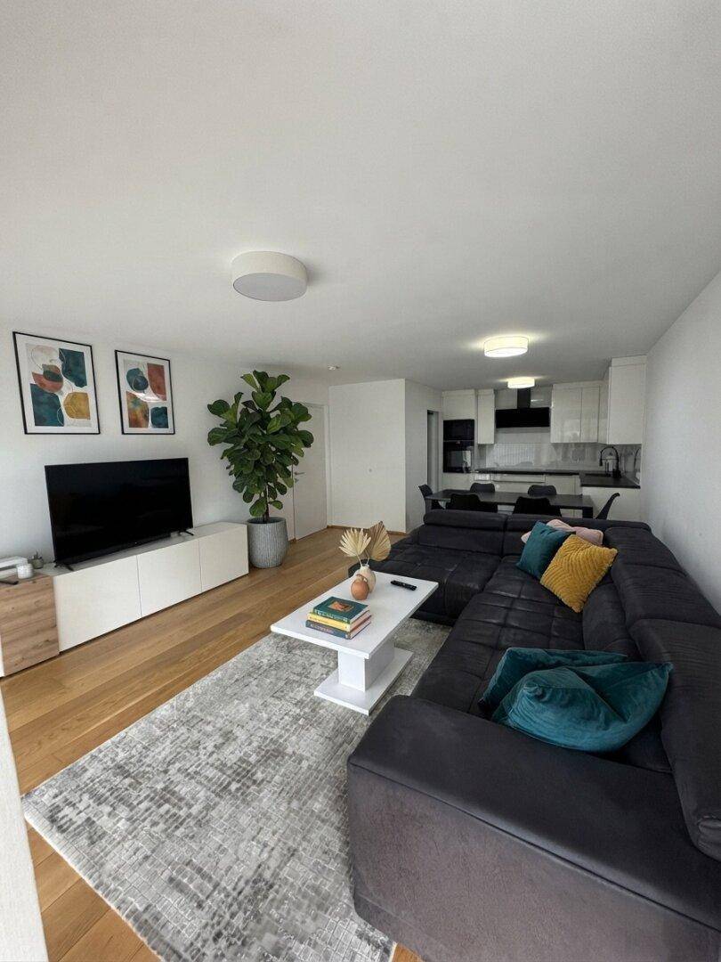 Geräumiges Wohnzimmer mit großem Ecksofa, Fernseher und offener Verbindung zur Küche.