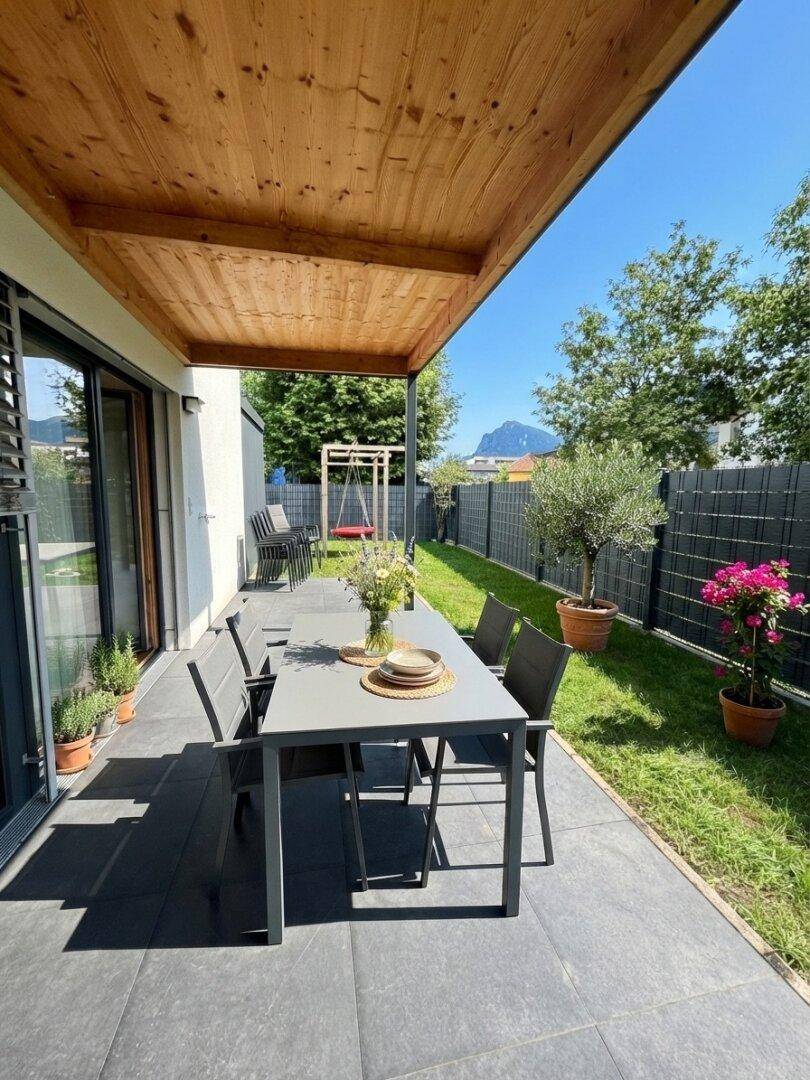 Sonniger Terrassenbereich mit Esstisch, Holzüberdachung und Blick auf die Berge.