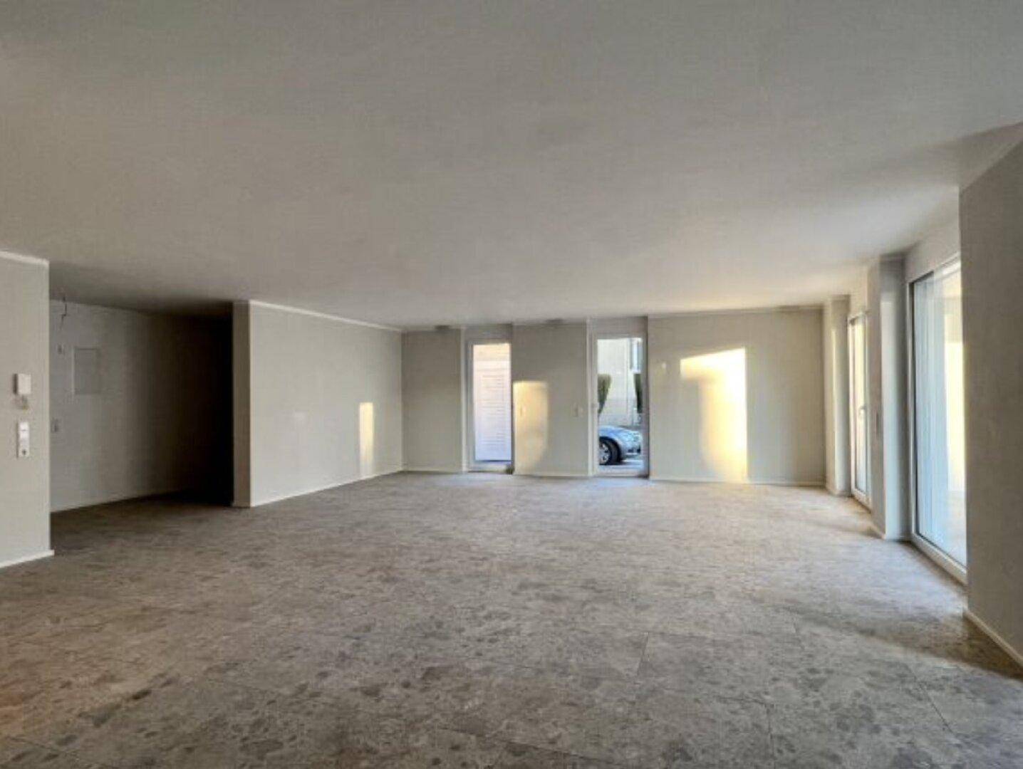 Heller, unmöblierter Raum mit großen Fensterfronten, die viel Sonnenlicht in den Innenbereich lassen.