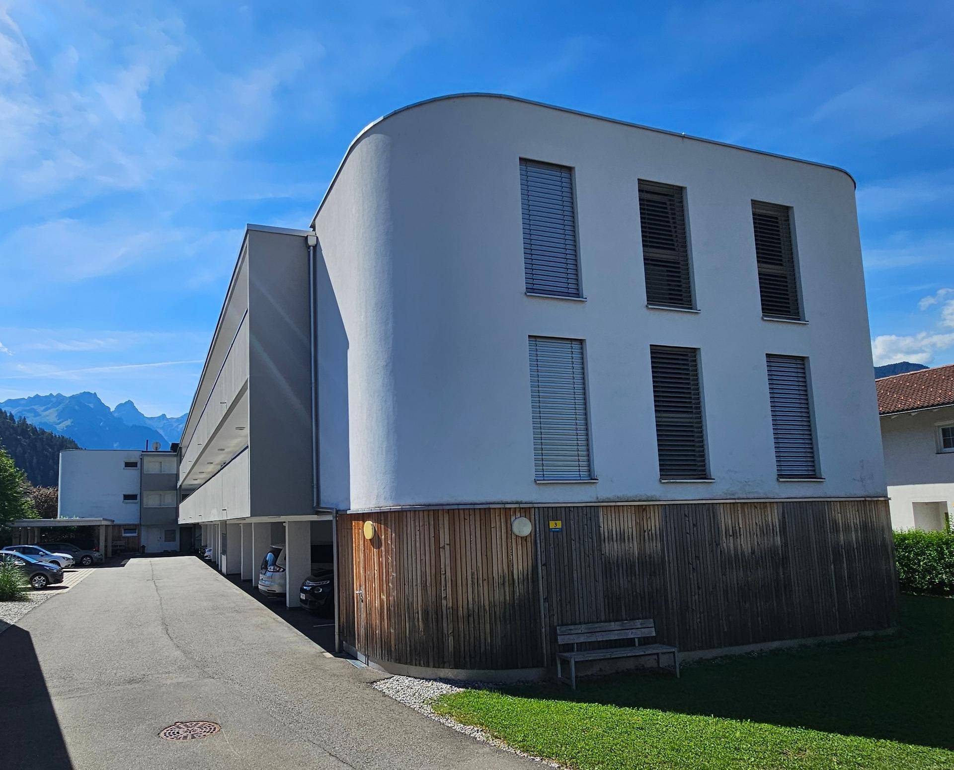 Moderne Architektur des Gebäudes mit abgerundeter Ecke, Parkplätzen und Bergblick.
