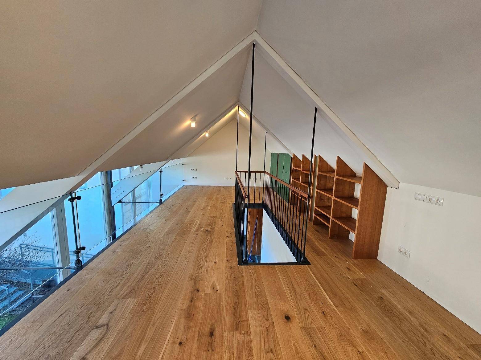 Offener Loftbereich mit Holzboden, Dachschrägen und Glasgeländer, bietet vielseitige Nutzung.