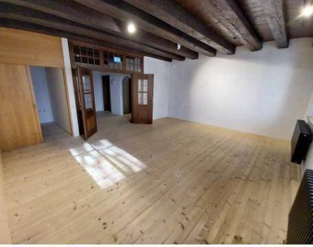 Geräumiger Innenraum mit sichtbaren Holzbalken an der Decke und einem hellen Holzplankenboden.