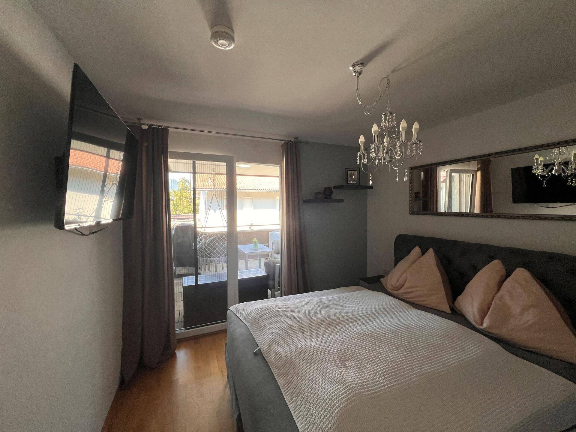 Schlafzimmer mit großem Bett, Kronleuchter, Spiegel und Zugang zum Balkon.
