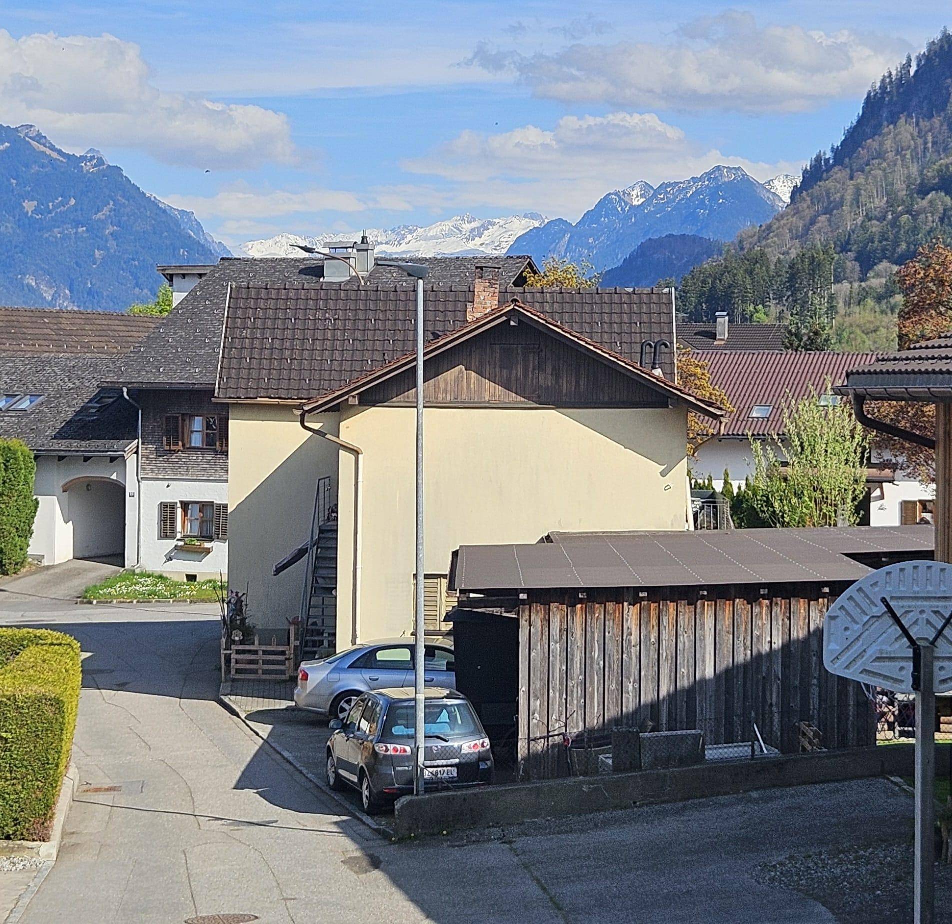 Seitenansicht eines Hauses mit geparkten Autos und einer beeindruckenden Bergkulisse im Hintergrund.