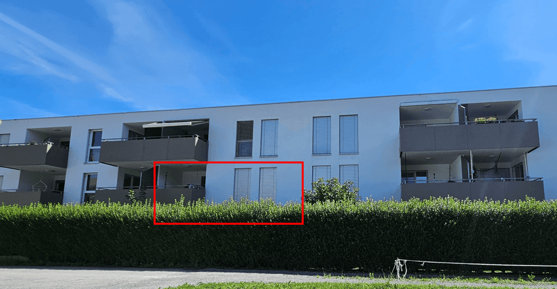 Ansicht der modernen Wohnanlage mit Balkonen und einer grünen Hecke vor der Fassade.