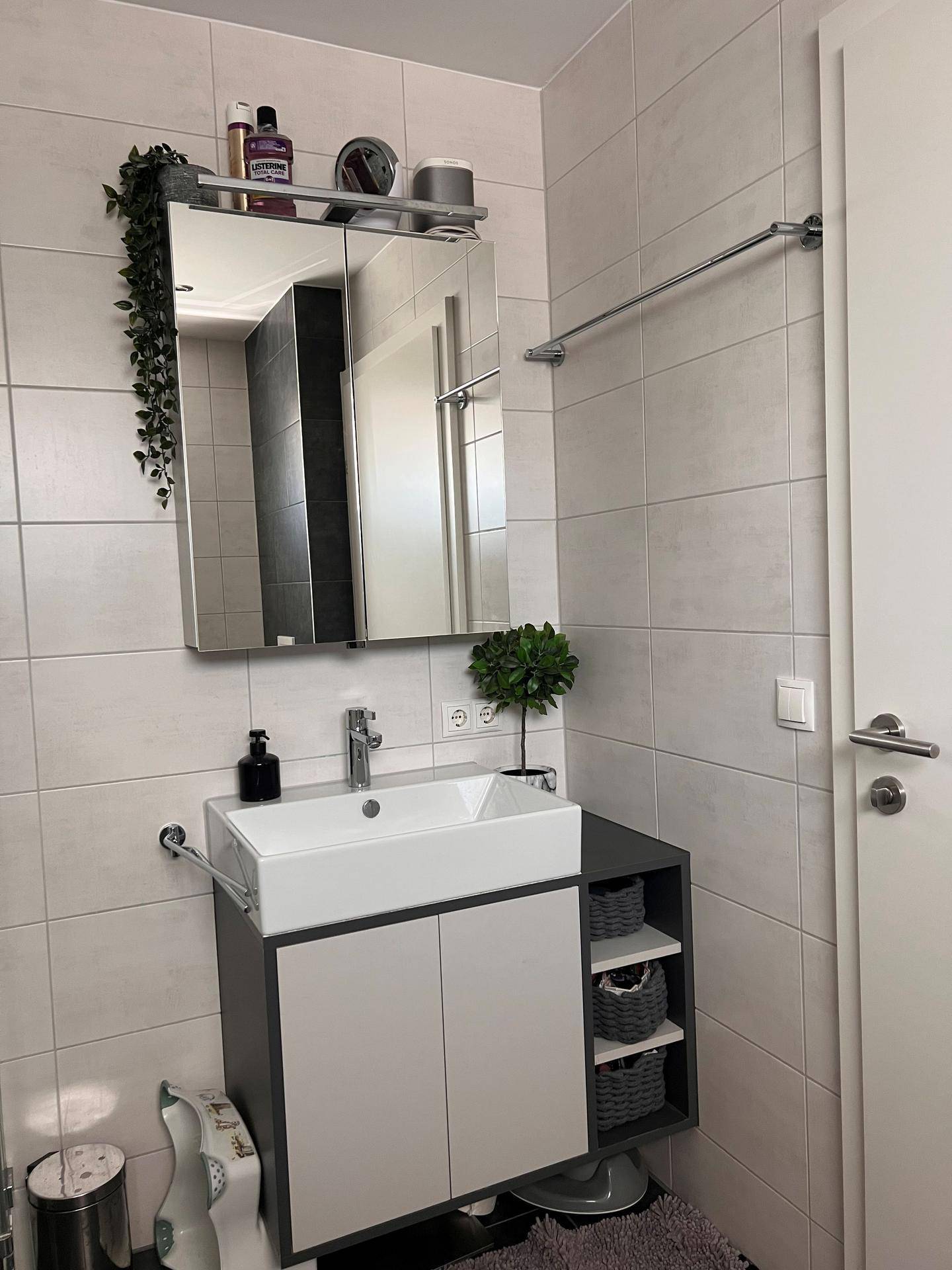 Modernes Badezimmer mit Waschtisch, Spiegelschrank und hellen Fliesen.