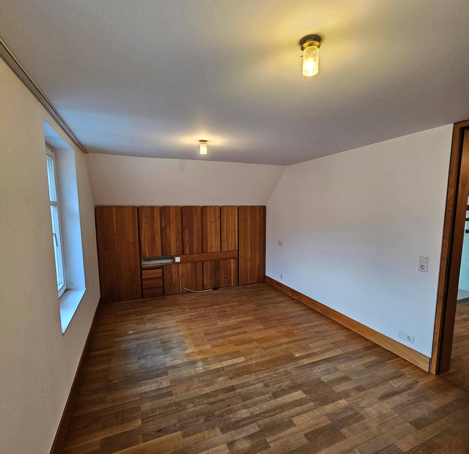 Helles Schlafzimmer mit Holzboden, Dachschräge und integrierten Holzschränken.