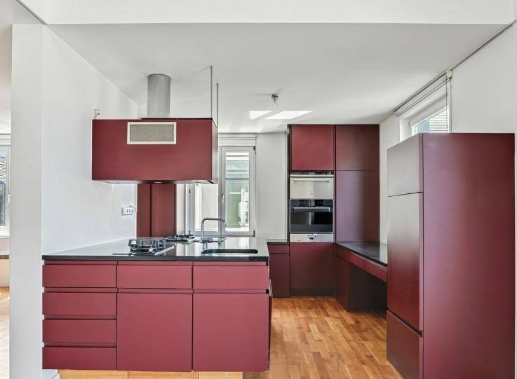 Moderne Küche in Bordeauxrot mit Kochinsel, integrierten Geräten und Holzboden.