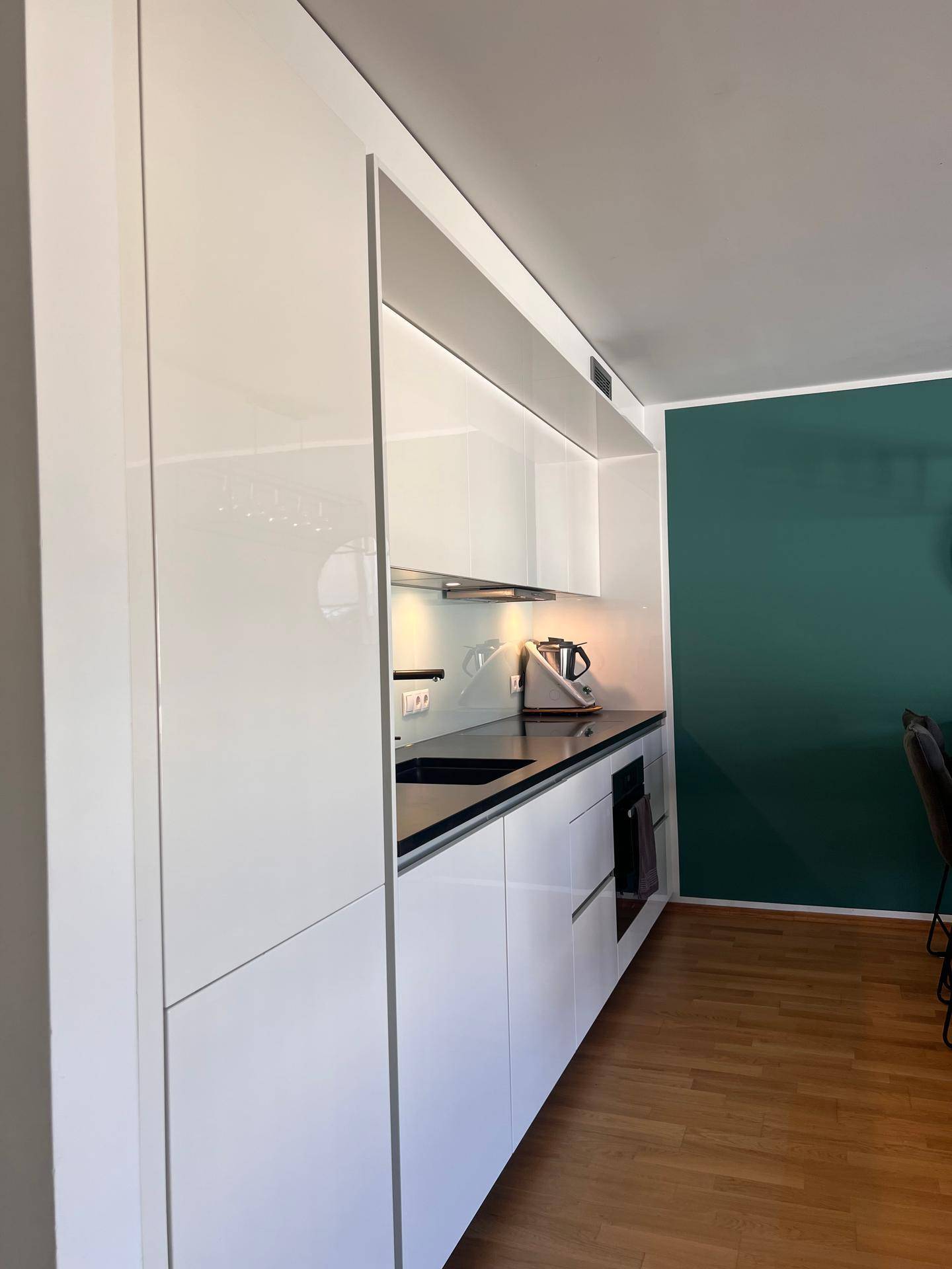 Moderne Einbauküche mit weißen Hochglanzfronten und dunkler Arbeitsplatte.