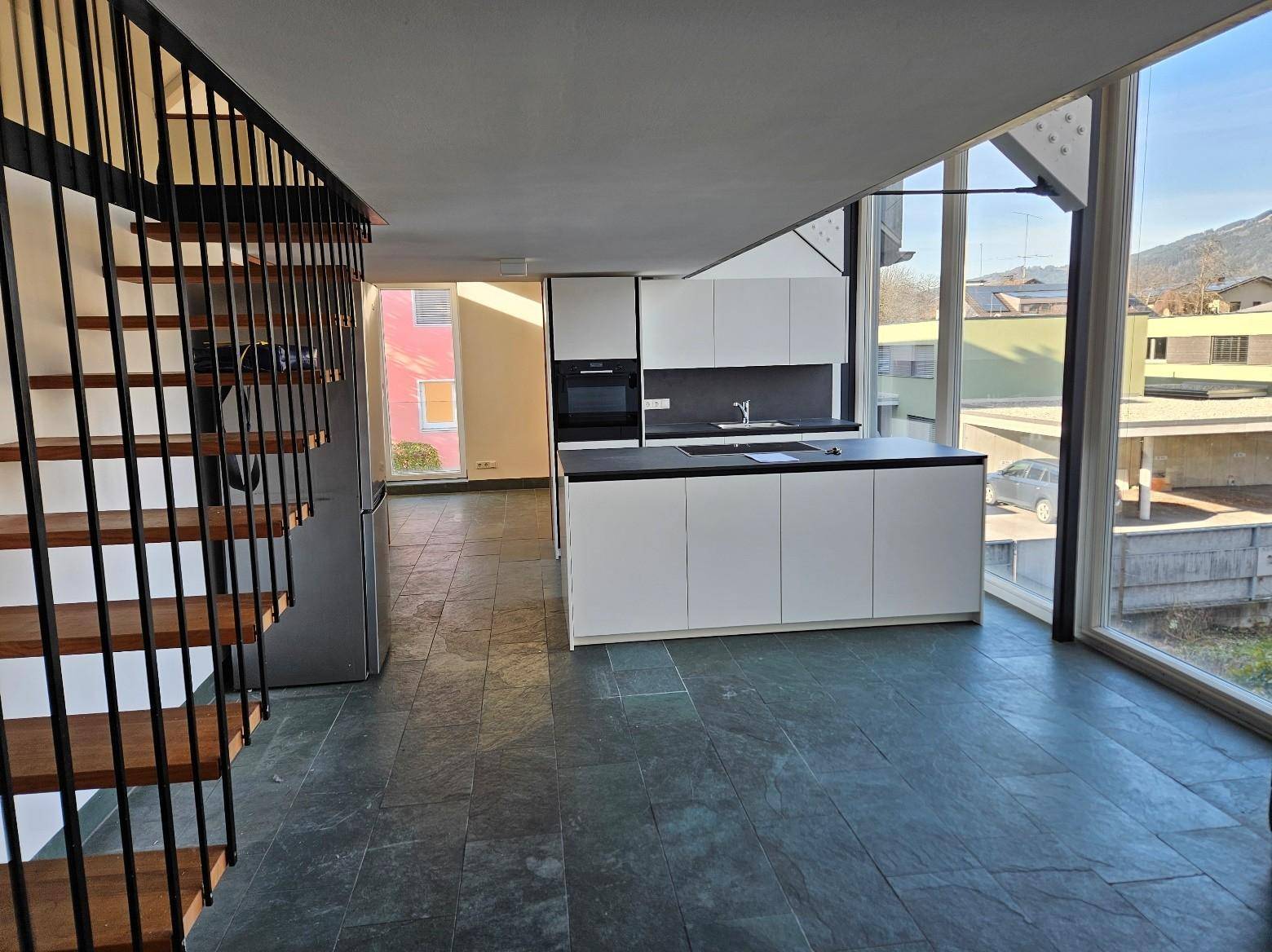 Moderne offene Küche mit Kochinsel und dunklen Fliesen, verbunden mit einem Treppenhaus.