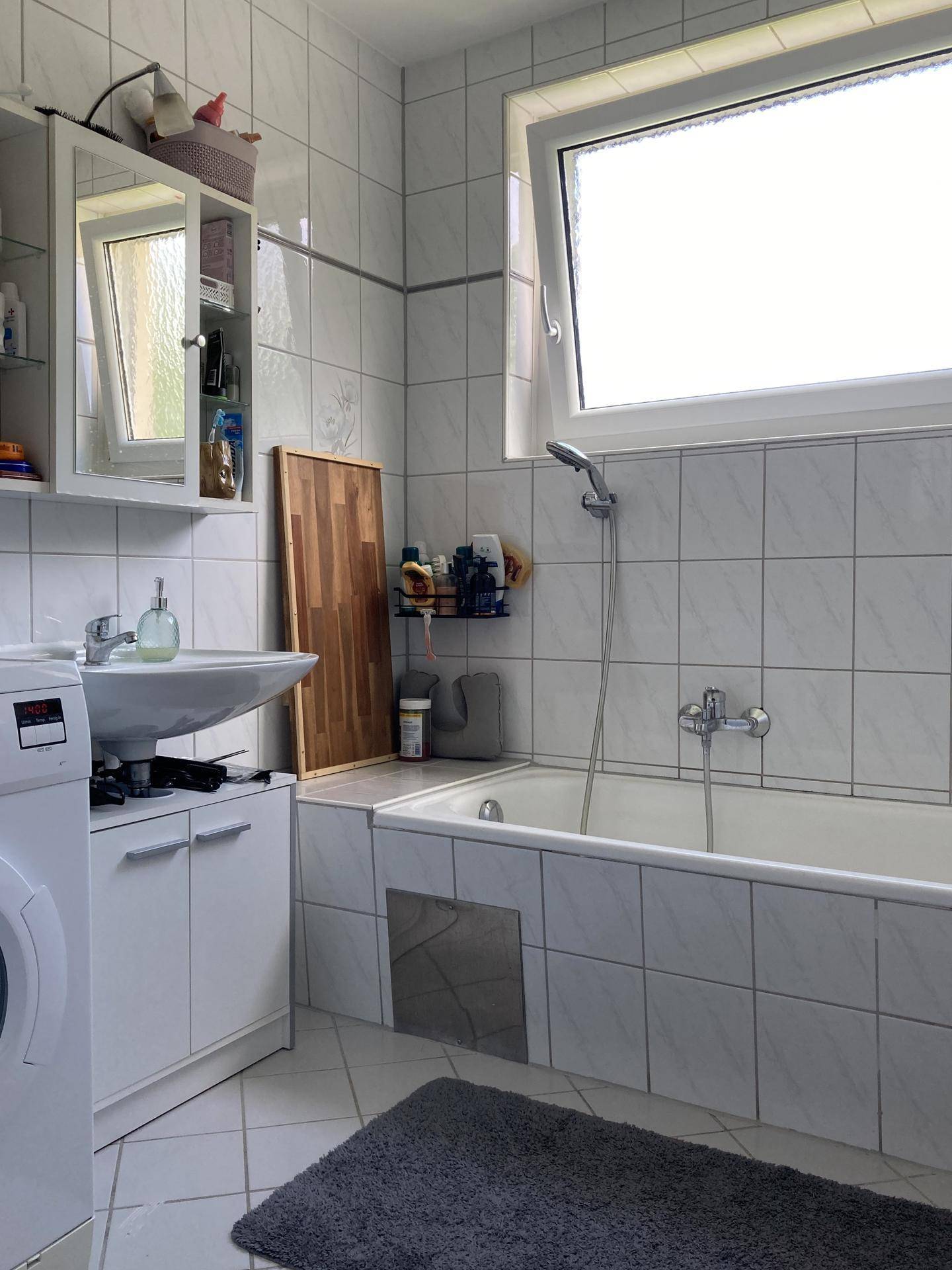 Gefliestes Badezimmer mit Badewanne, Waschbecken und Fenster für Tageslicht.