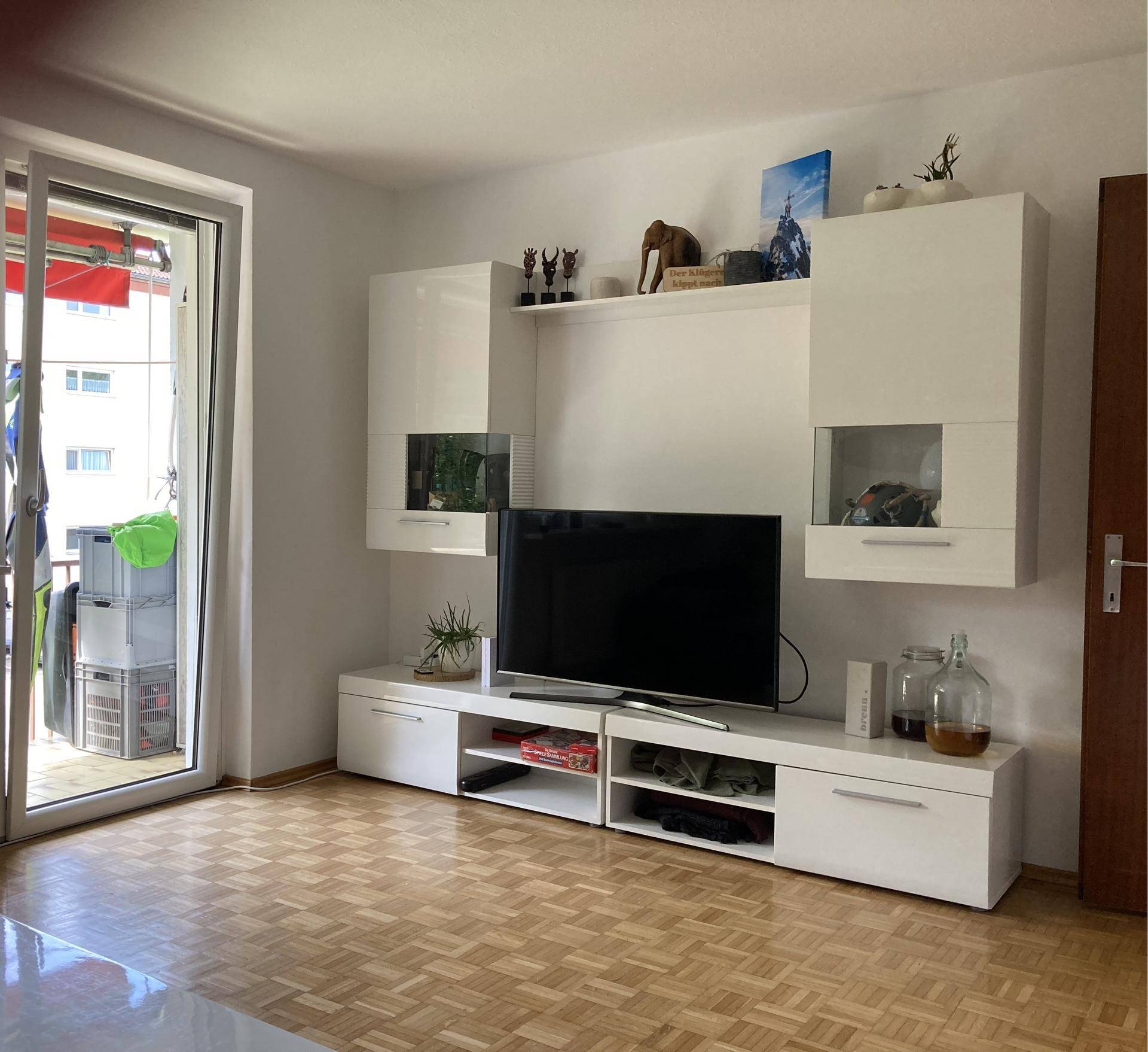 Wohnzimmer mit modernem TV-Möbel, Parkettboden und Zugang zu einem Balkon.