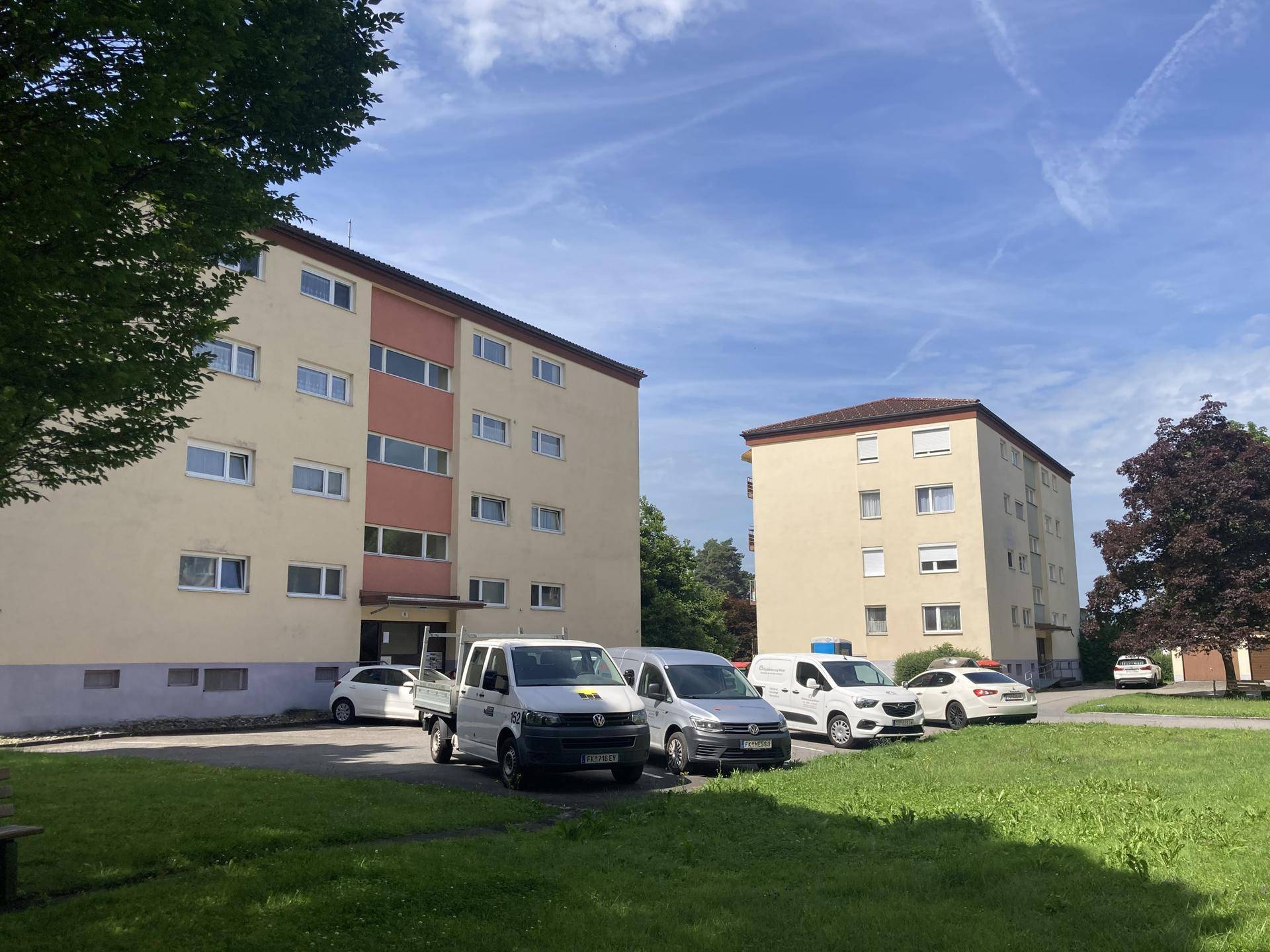 Wohnanlage mit mehreren Gebäuden, Parkplätzen und Grünflächen an einem sonnigen Tag.