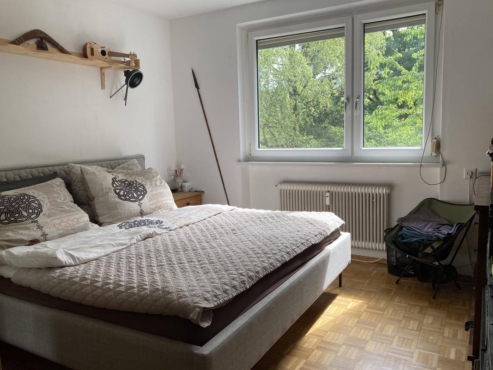Schlafzimmer mit Doppelbett, Parkettboden und großem Fenster mit Blick ins Grüne.