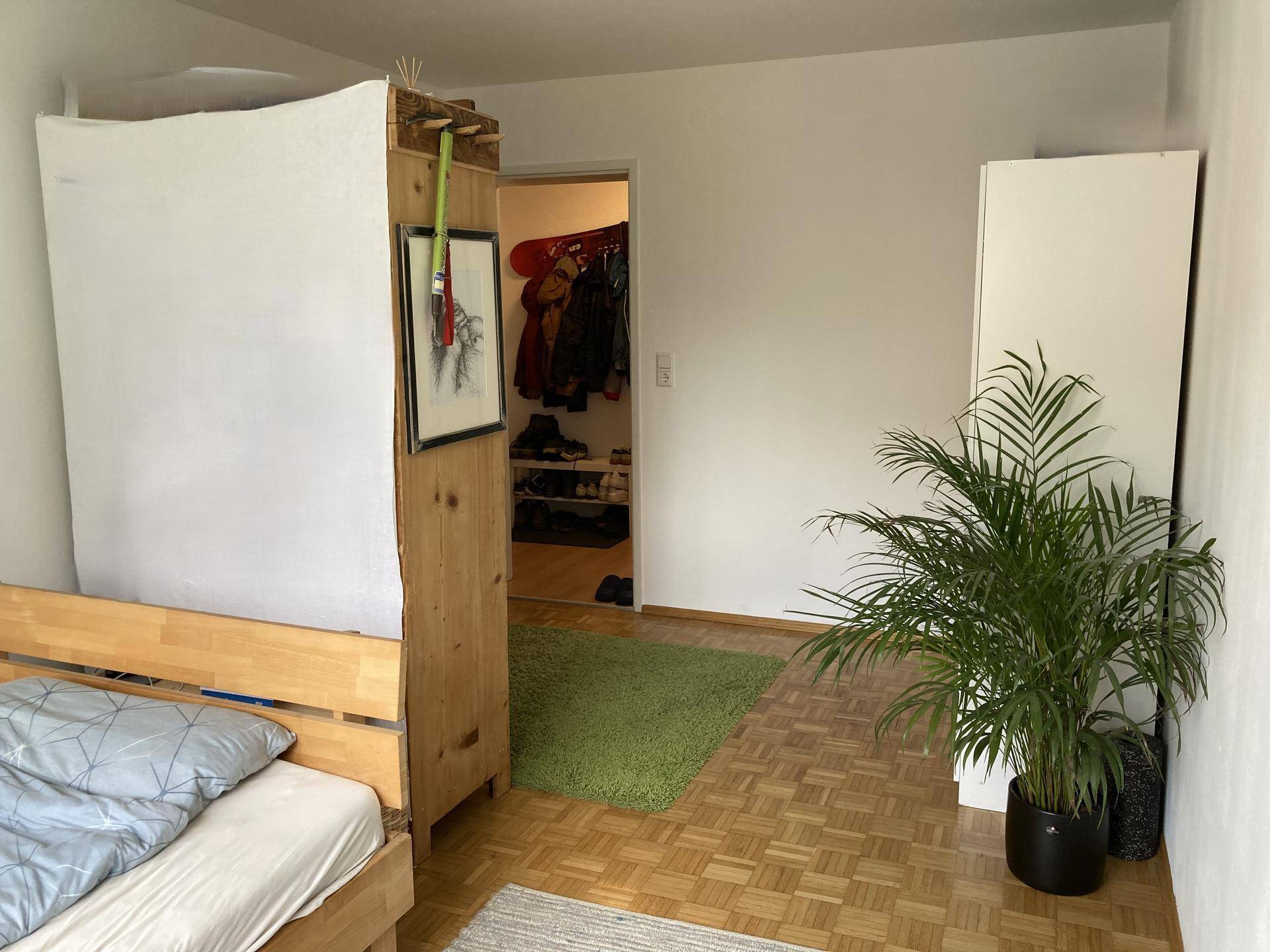 Schlafzimmer mit Holzbett, Kleiderschrank und grünem Teppich auf Parkettboden.