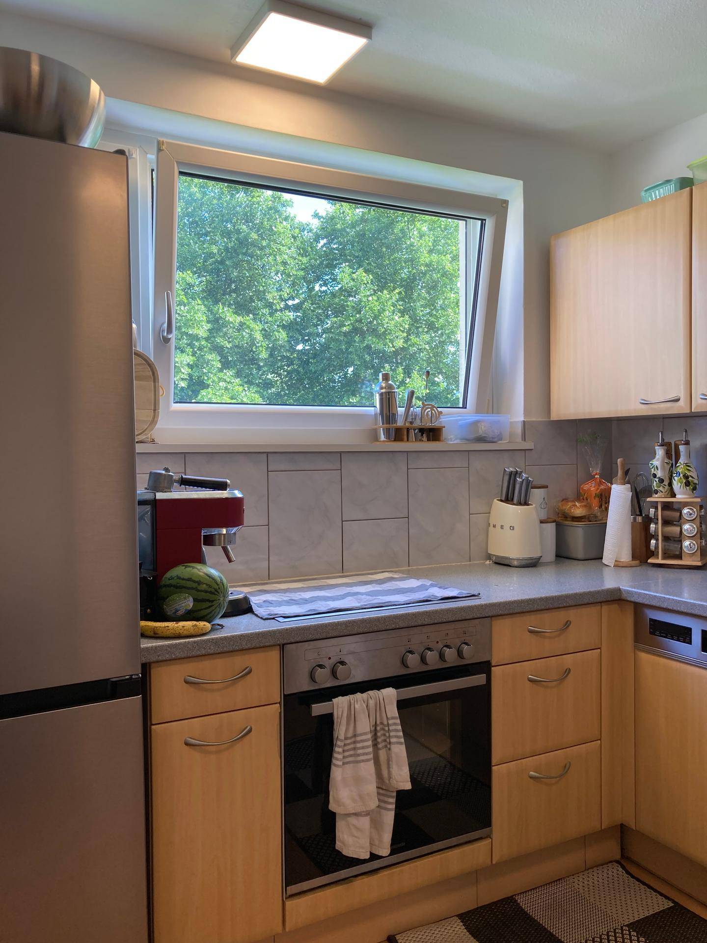 Funktionale Küche mit hellen Holzschränken, integriertem Backofen und Fenster mit Blick ins Grüne.