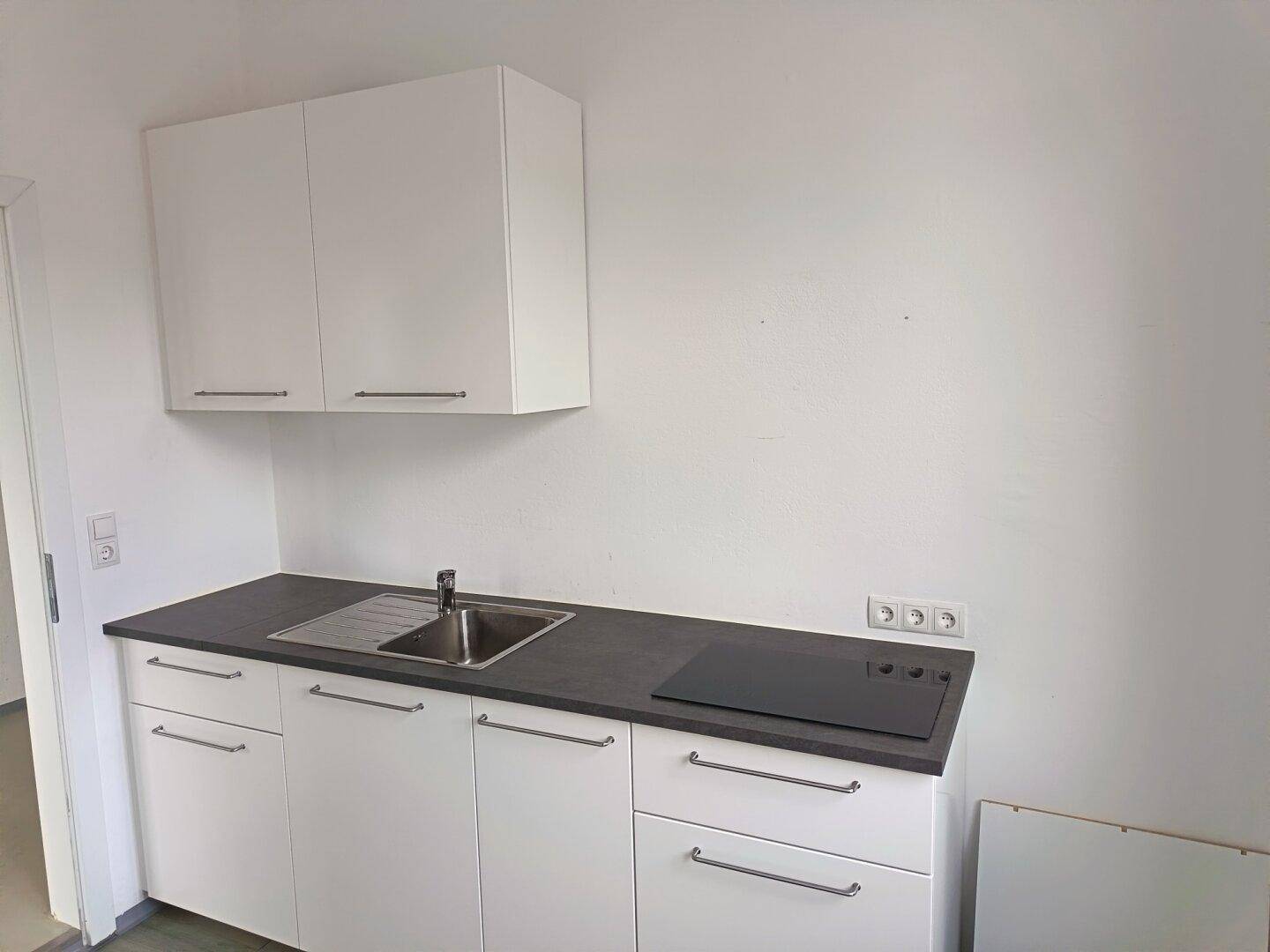 Moderne Küchenzeile mit weißen Schränken, Spüle und Induktionskochfeld, ideal für kleine Wohnungen.
