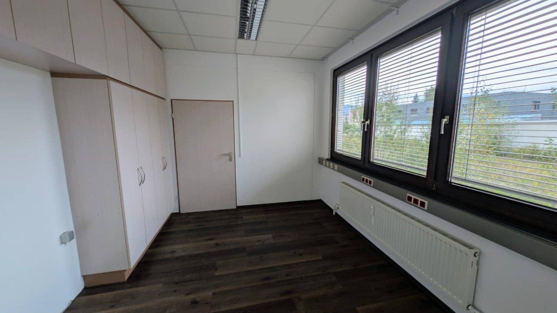 Leeres Büro mit Einbauschränken, dunklem Boden und großen Fenstern, bereit zur Gestaltung.