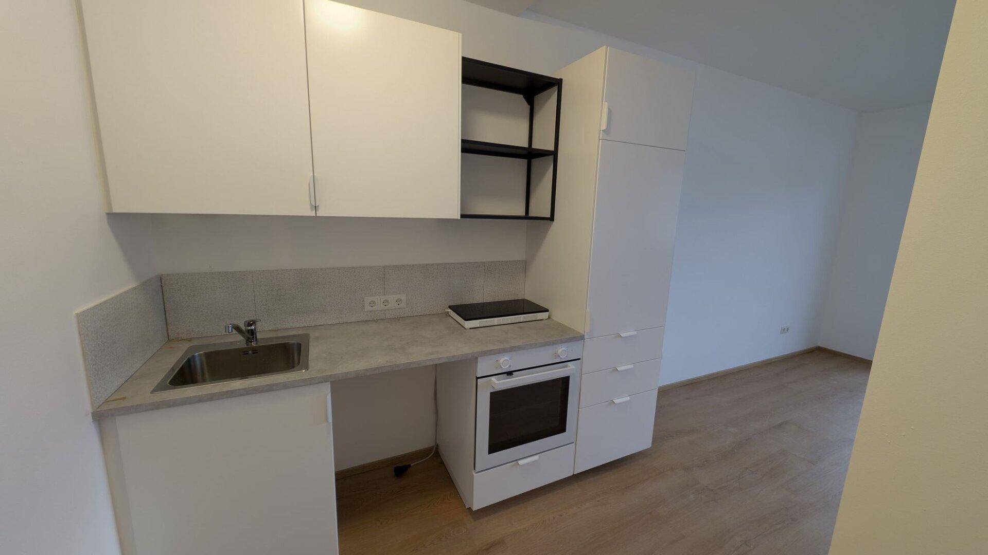 Kompakte Küchenzeile mit weißen Schränken, Spüle, Backofen und Kochfeld, ideal für kleine Haushalte.
