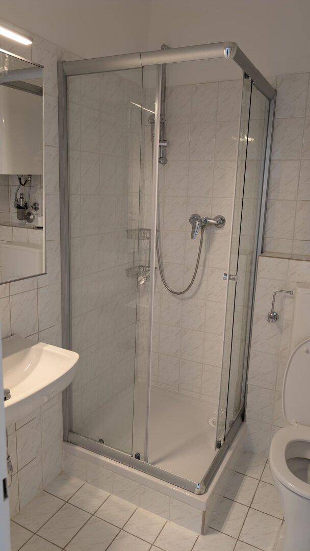 Modernes Badezimmer mit Duschkabine, Waschbecken und WC, komplett gefliest.