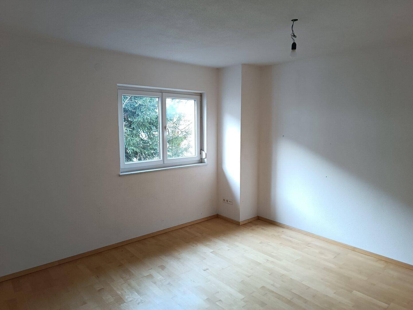 Schlafzimmer mit hellem Parkettboden und großem Fenster, das viel Tageslicht hereinlässt.