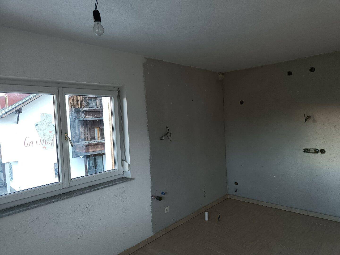 Unfertige Küche mit vorbereiteten Anschlüssen und einem Fenster mit Blick auf die Umgebung.
